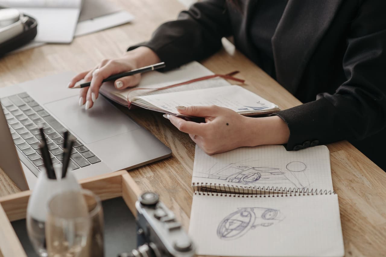 A desk with a laptop, sketches and a notebook held open