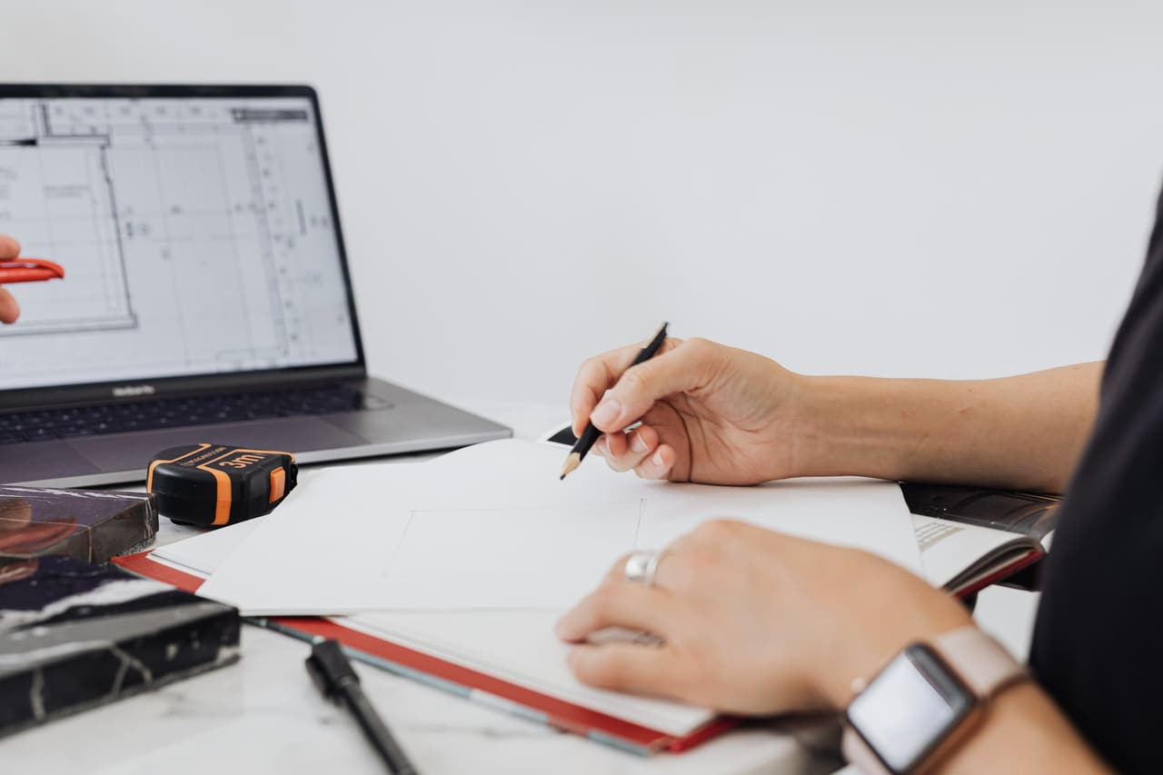 Close-up of a hand writing planning notes beside a laptop